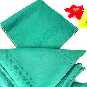 May include: A set of four green linen napkins with a subtle embossed pattern. The napkins are folded in a triangle shape.