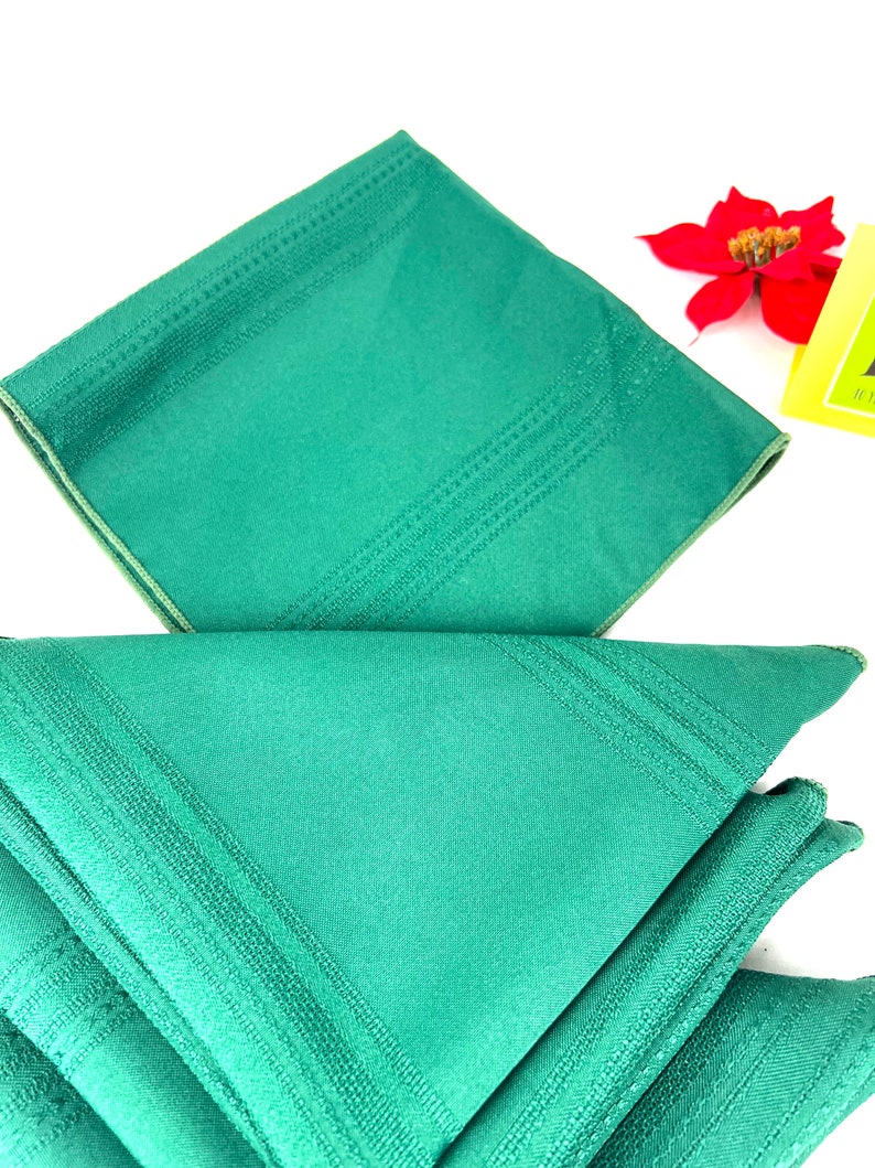 May include: A set of four green linen napkins with a subtle embossed pattern. The napkins are folded in a triangle shape.