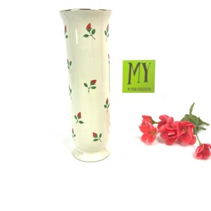 May include: A white ceramic vase with a gold rim and a pattern of red roses and green leaves. The vase is about 10 inches tall and has a round base.