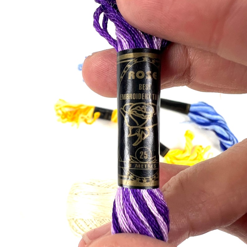 May include: A spool of purple and white embroidery thread with a black label that reads "ROSE BEST EMBROIDERY THREAD 25 METRES".