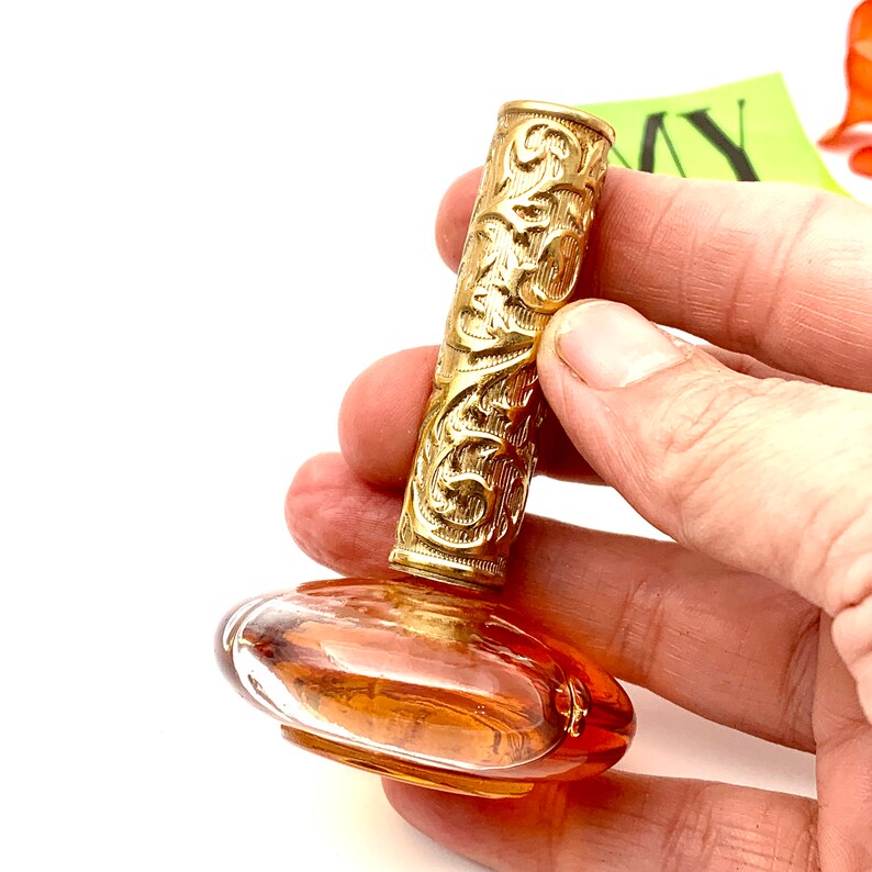 May include: A vintage perfume bottle with a gold, ornate, cylindrical stopper and a clear, amber-colored glass base.