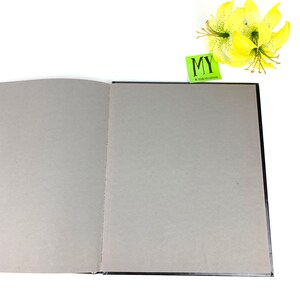 May include: A black hardcover book with a gray interior, open to a blank page. A green sticky note with the text "MY 50 YEAR COLLECTION" is visible on the top right corner of the book.