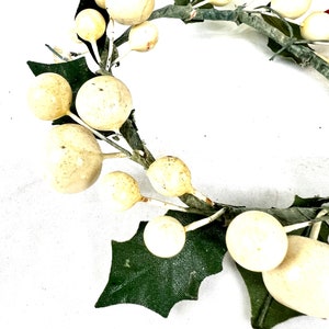 May include: A white and green Christmas wreath with white berries and green holly leaves.