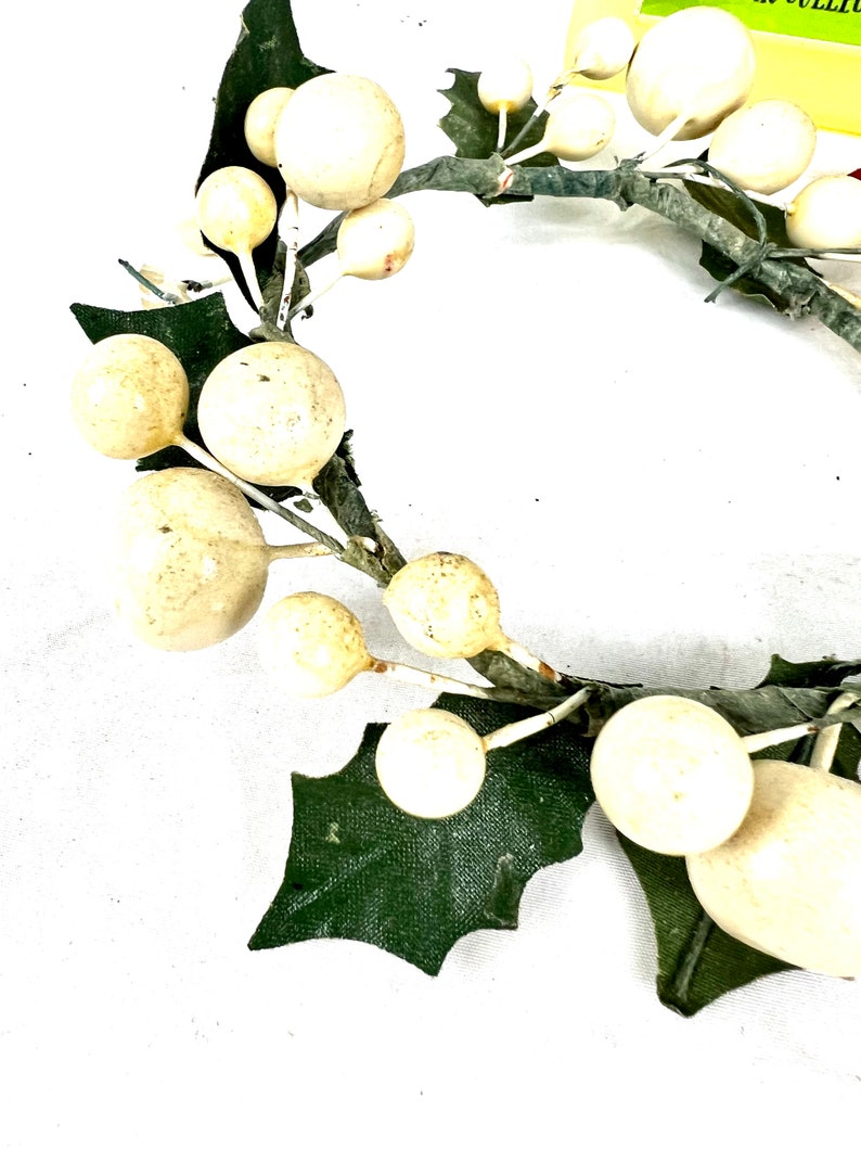 May include: A white and green Christmas wreath with white berries and green holly leaves.