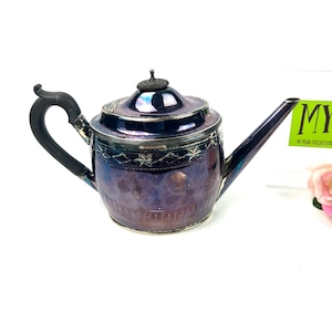 May include: A silver teapot with a black wooden handle and a decorative design. The teapot has a shiny, iridescent finish.