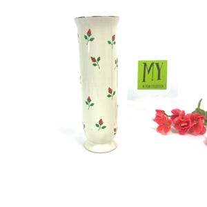 May include: A white ceramic vase with a gold rim and a pattern of red and green roses. The vase is about 10 inches tall and has a classic design.