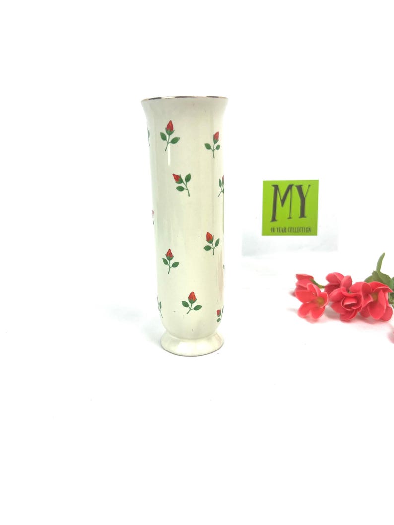 May include: A white ceramic vase with a gold rim and a pattern of red and green roses. The vase is about 10 inches tall and has a classic design.