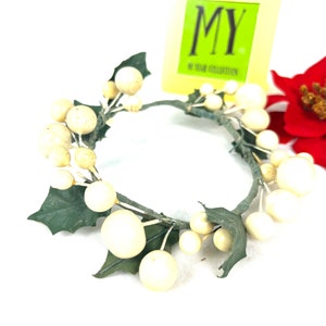 May include: A white and green artificial wreath with white berries and green leaves. The wreath is made of wire and is about 10 inches in diameter. The wreath is sitting on a white surface. The text "MY YEAR COLLECTION" is visible on a yellow tag.