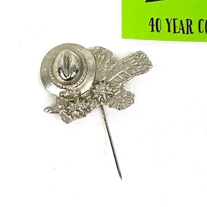 May include: Silver-toned pin featuring a hat with a feather and leaves. The pin is attached to a long, thin pin.