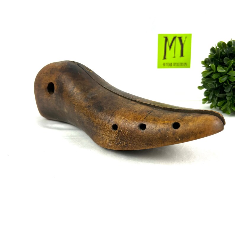 May include: A wooden shoe stretcher with a brown finish and multiple holes. The stretcher is designed to help maintain the shape of shoes.