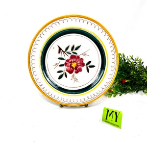 May include: A white ceramic plate with a green and gold border and a single pink flower with green leaves in the center.