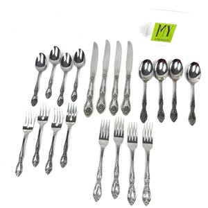 May include: A collection of ornate silverware, including spoons, forks, and knives, arranged on a white background. The silverware has a floral design on the handles. A small green and white tag is in the upper right corner.