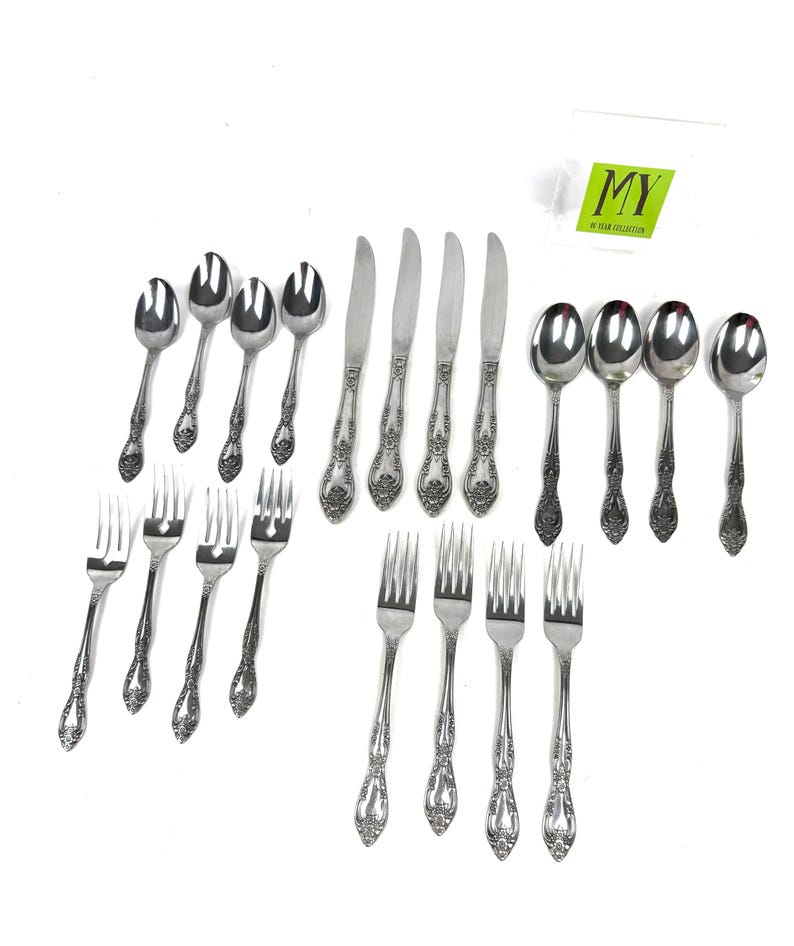 May include: A collection of ornate silverware, including spoons, forks, and knives, arranged on a white background. The silverware has a floral design on the handles. A small green and white tag is in the upper right corner.