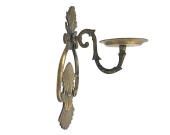 May include: A gold metal wall sconce with a decorative scroll design. The sconce has a round plate for holding a candle or other decorative item.
