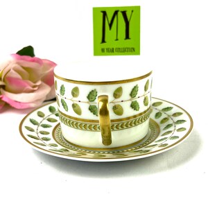 May include: A white porcelain teacup and saucer with a green and gold floral pattern. The cup has a gold handle and the saucer has a gold rim. The text "MY 50 YEAR COLLECTION" is on a green tag.