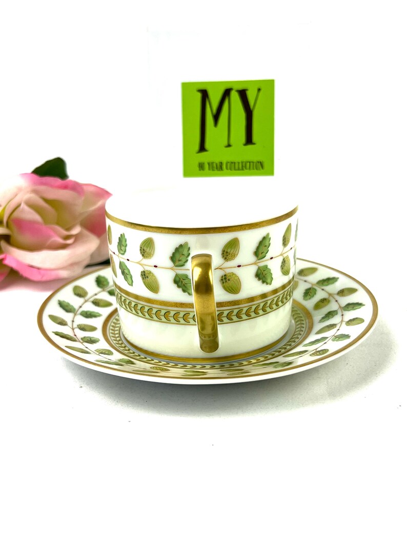 May include: A white porcelain teacup and saucer with a green and gold floral pattern. The cup has a gold handle and the saucer has a gold rim. The text "MY 50 YEAR COLLECTION" is on a green tag.