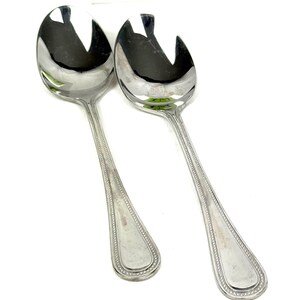 May include: Two shiny, silver serving spoons with a slotted design. The spoons have a teardrop-shaped bowl and a long handle with a beaded border. The spoons are likely for serving salad or other dishes.