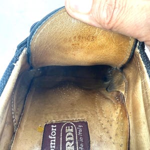 May include: Close-up of the inside of a dark blue shoe. The interior is tan leather with a brown label that reads "VERDE made in italy". The shoe's interior shows signs of wear.