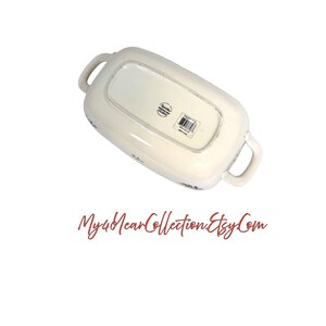 Pu&ograve; includere: Piatto da portata rettangolare bianco sporco con due manici. Il lato inferiore del piatto &egrave; visibile, con l'etichetta del produttore e un motivo floreale. Il piatto ha un aspetto leggermente invecchiato.