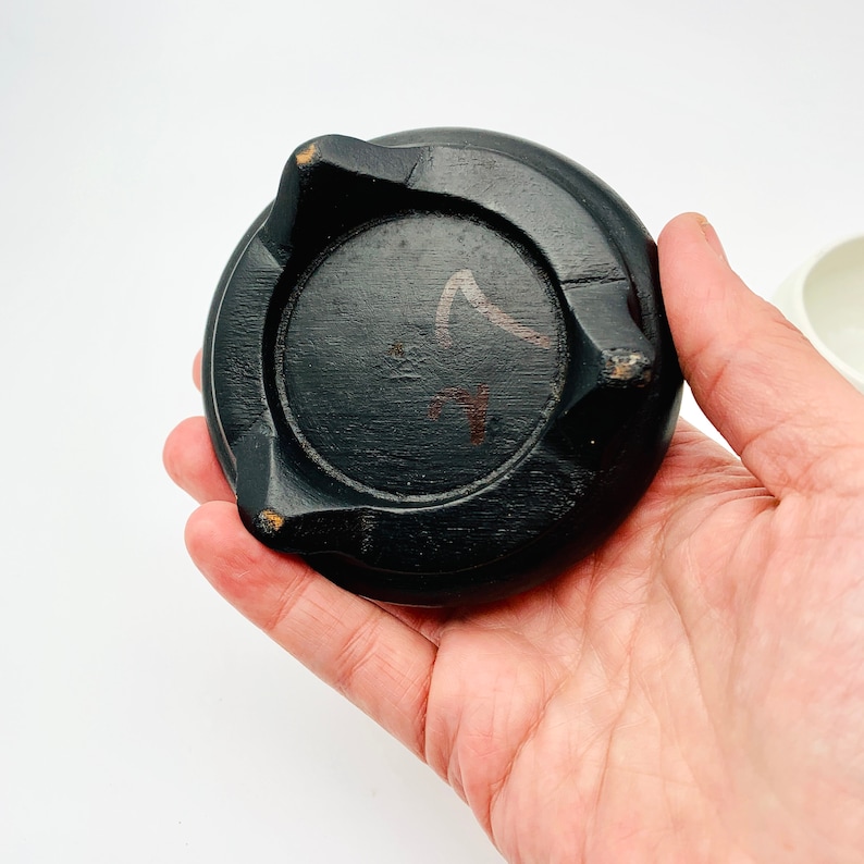 May include: Black wooden base with three legs and a circular top. The base has a handwritten number "7" on the top.