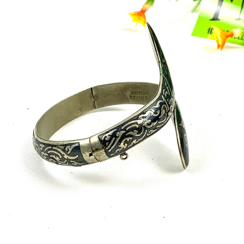 May include: A silver bangle bracelet with a black enamel design and a hinged opening. The bracelet is engraved with "STERLING SILVER 925".
