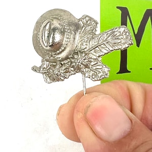 May include: A silver pin with a detailed design of a round fruit with leaves. The pin is attached to a thin metal rod.