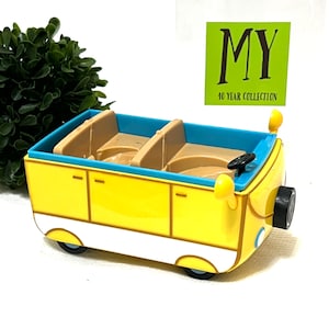 May include: A yellow toy car with a blue top and tan seats. The car has black wheels, a black steering wheel, and side mirrors. The text "MY 40 YEAR COLLECTION" is on a green square in the background.