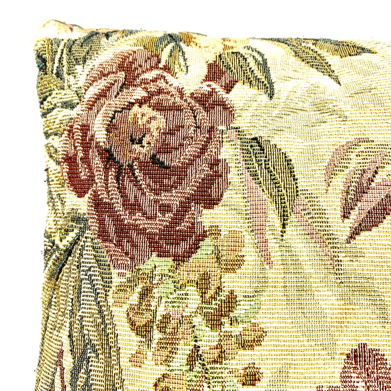 May include: A close-up of a decorative pillow with a floral pattern. The pillow is made of a woven fabric with a textured surface. The pattern features a large red rose with green leaves and a smaller floral design in the background.