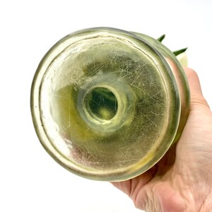 May include: The bottom of a clear glass vase with a green tint. The vase has a round base and a smooth, slightly textured surface.