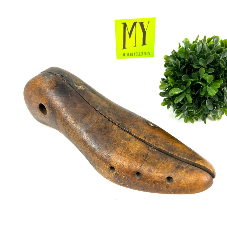 May include: A vintage wooden shoe stretcher with a split design and multiple holes. The stretcher is brown and has a worn appearance.