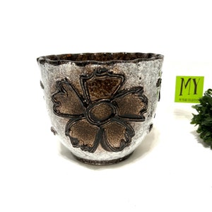 Peut inclure: Un pot en céramique blanche avec un motif de fleur marron. Le pot a un bord festonné et une surface texturée.