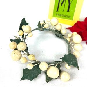 May include: A white and green artificial holly wreath with white berries. The wreath is made of wire and has a simple design.