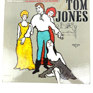 Puede incluir: Funda de vinilo vintage para "Tom Jones", una producci&oacute;n musical. La portada presenta una ilustraci&oacute;n estilizada de personajes en colores vibrantes: un hombre en blanco y azul, dos mujeres en amarillo y rojo y una mujer en negro. El texto incluye "Theatre Productions" y "The Original Musical Cast Recording."