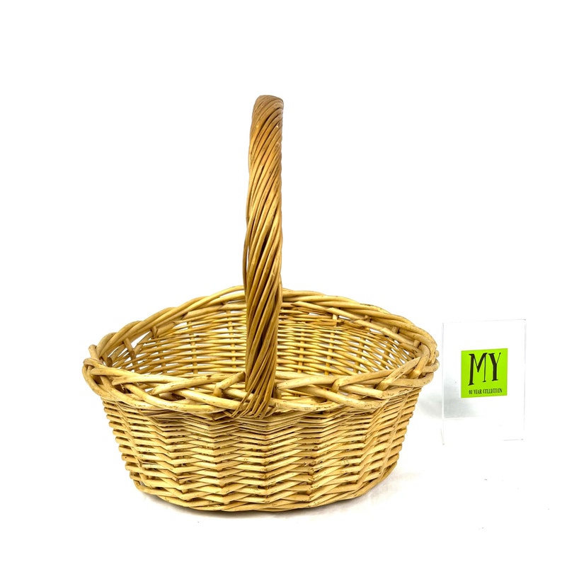 May include: A natural woven wicker basket with a single handle. The basket is oval shaped and has a light brown color.