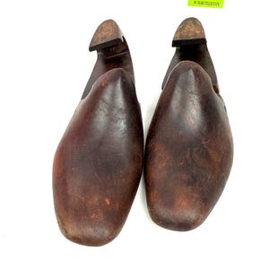 May include: Pair of vintage wooden shoe forms, featuring a dark brown, aged appearance. The forms have a rounded toe and a heel piece, with the text "MY 10 YEAR COLLECTION" on a yellow sticker.