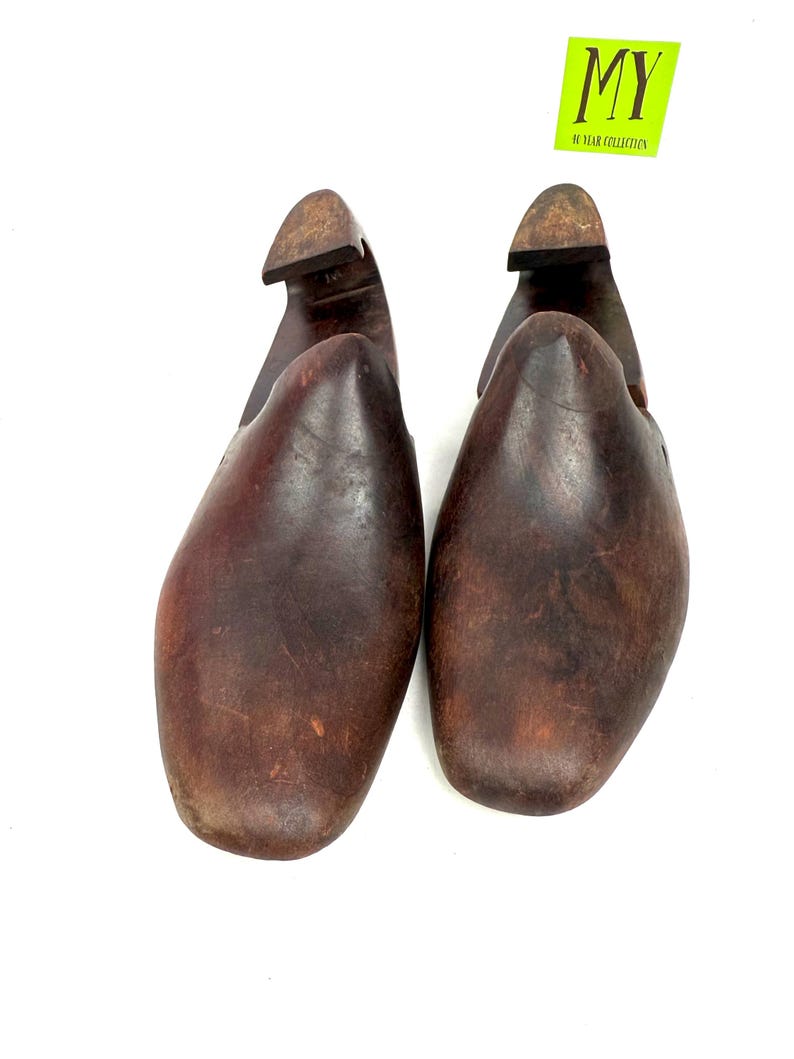 May include: Pair of vintage wooden shoe forms, featuring a dark brown, aged appearance. The forms have a rounded toe and a heel piece, with the text "MY 10 YEAR COLLECTION" on a yellow sticker.
