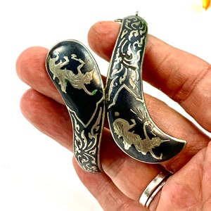 May include: A pair of silver bracelets with black enamel and intricate silver filigree designs. The bracelets feature a stylized animal design.