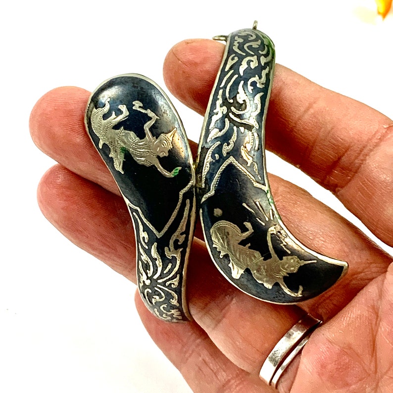 May include: A pair of silver bracelets with black enamel and intricate silver filigree designs. The bracelets feature a stylized animal design.