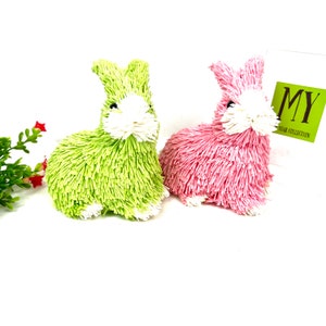 Op de afbeelding: Twee pluche paashazenfiguren, een groene en een roze, met witte gezichten. De hazen zitten op een wit oppervlak. De tekst "MY YEAR COLLECTION" is zichtbaar op een witte kaart achter de hazen.