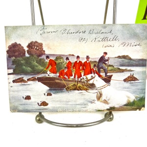 K&ouml;nnte beinhalten: Eine antike Postkarte, die eine Gruppe von M&auml;nnern in roten M&auml;nteln und Zylindern zeigt, die Pferde durch einen Fluss f&uuml;hren. Die Postkarte tr&auml;gt den Titel "Crossing the Stream" und ist signiert mit "From Theodore Breland, (P.O.) Kittrell, (state) Miss."