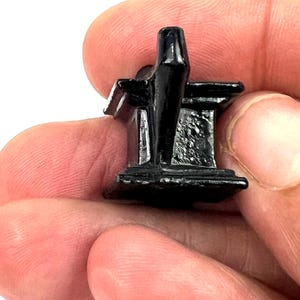 May include: A small, black, plastic miniature of a church building. The church has a pointed roof and a cross on top.