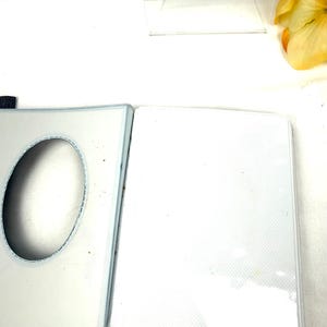 Peut inclure: Un album photo blanc ouvert avec une bordure bleu clair. L'album a une grande d&eacute;coupe ovale sur la couverture avant. Les pages int&eacute;rieures sont blanches et semblent &ecirc;tre faites d'un mat&eacute;riau textur&eacute;. L'album est sur une surface blanche.