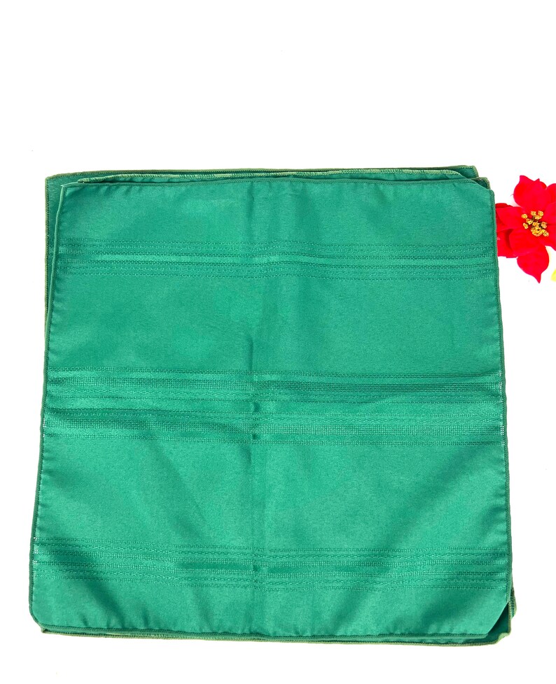 May include: A set of four green dinner napkins with a subtle striped pattern. The napkins are folded and stacked on a white background.
