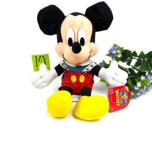 Vintage Mattel Mickey’s Stuff for Kids plush toy sitting upright with yellow shoes and original tag, displayed against a white background with flowers