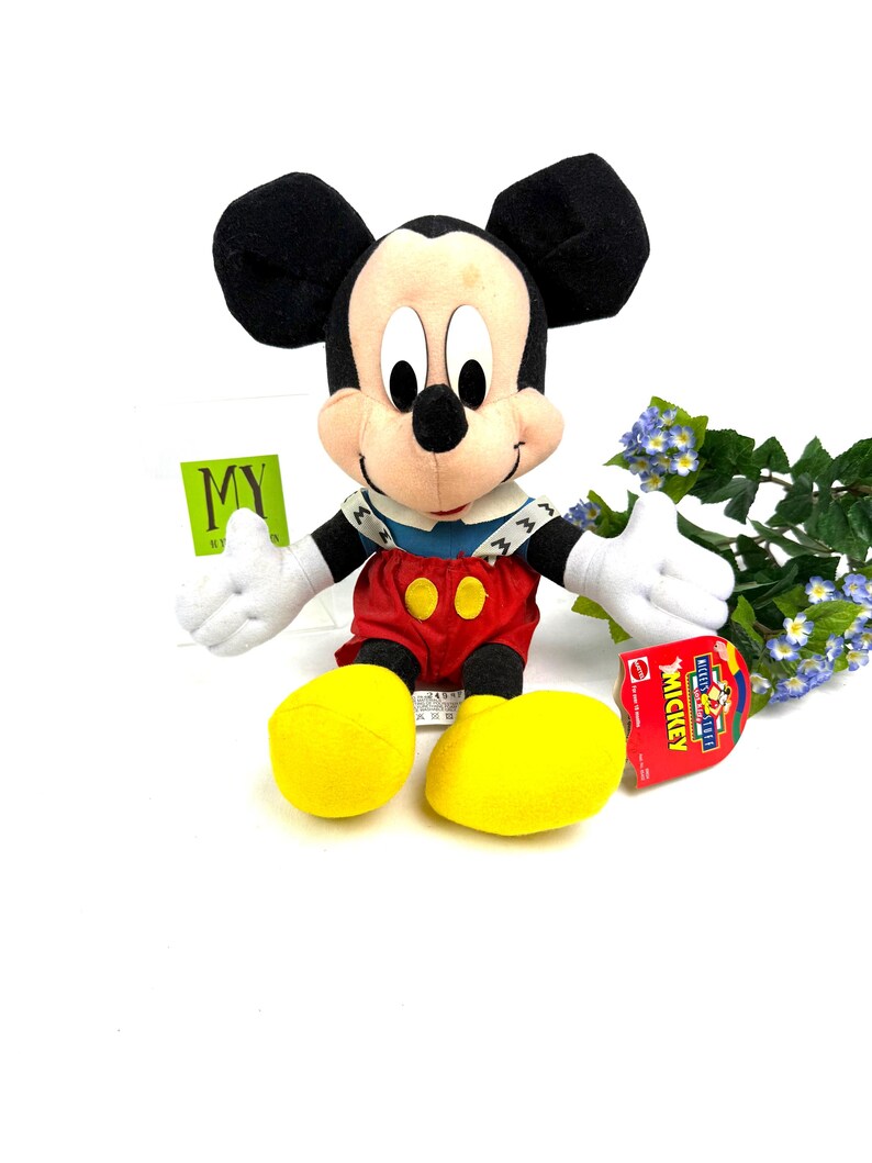 Vintage Mattel Mickey’s Stuff for Kids plush toy sitting upright with yellow shoes and original tag, displayed against a white background with flowers