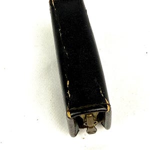 May include: A black leather case with a brass zipper closure. The rectangular case is slightly worn, with visible stitching and wear on the edges. The zipper is a vintage style, adding to the overall aesthetic.