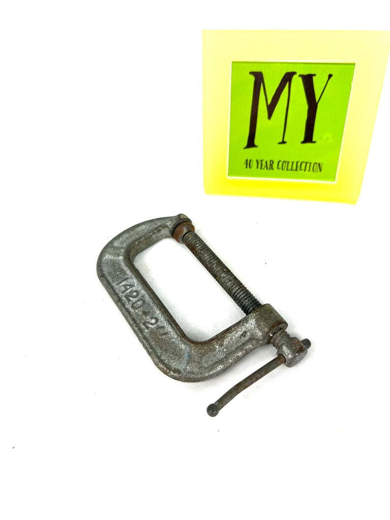 May include: A silver metal C-clamp with a handle and a screw. The clamp is marked "1420 21".