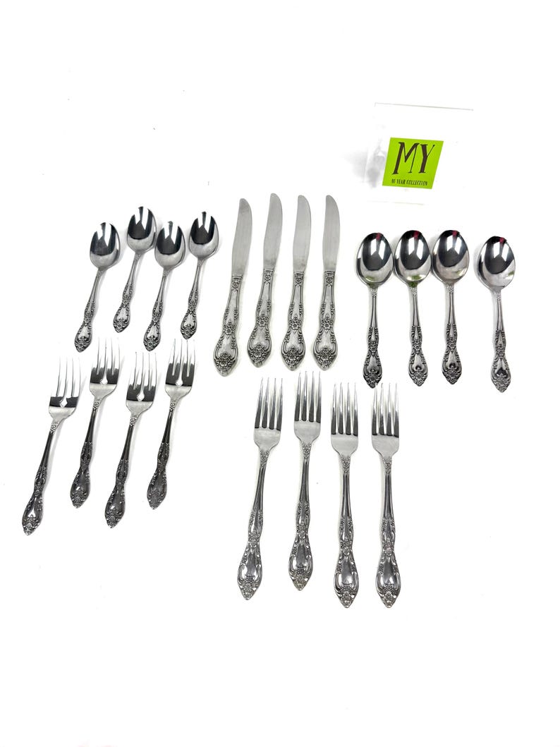 May include: A collection of vintage silverware, including spoons, forks, and knives, arranged on a white surface. The silverware features ornate floral detailing on the handles. The image includes the text "MY" in a green rectangle.
