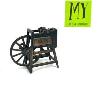 May include: A vintage metal pencil sharpener shaped like a spinning wheel. The sharpener is brown and has a small metal sign that reads "Playtime".