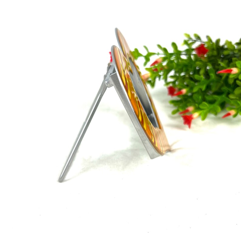 May include: A silver metal picture frame with a yellow and orange striped design. The frame is standing upright on a white surface.